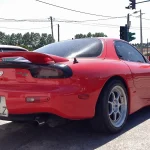 Red third-generation Mazda RX-7 FD coupe with a rear wing, seen from the rear three-quarter on a street
