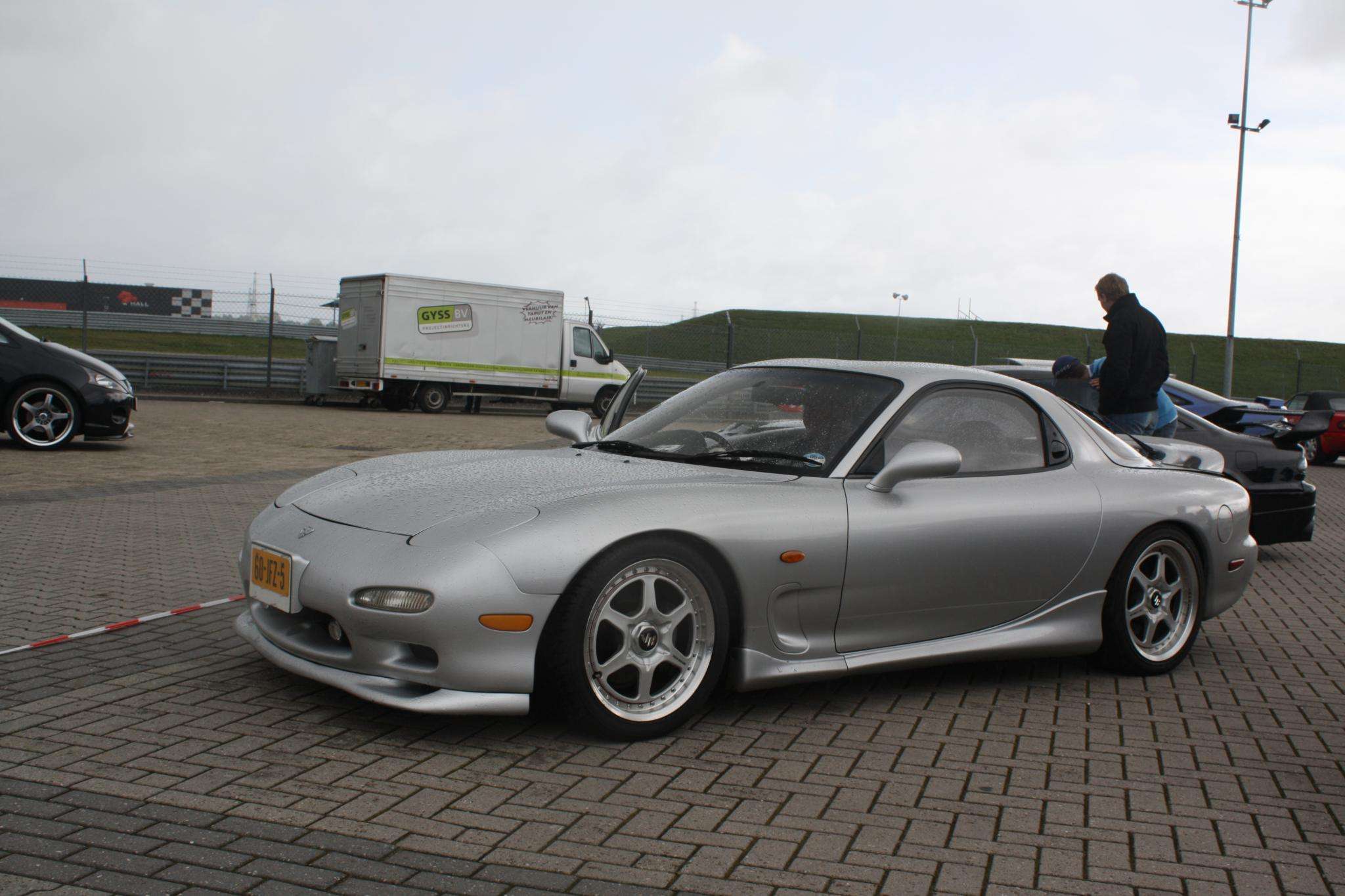 Silver third-generation Mazda RX-7 FD coupe parked on brick paving at a track event