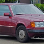 Burgundy 1991 Mercedes-Benz 300 CE-24 C124 coupe seen from the front three-quarter, showing the standard narrow-body shape
