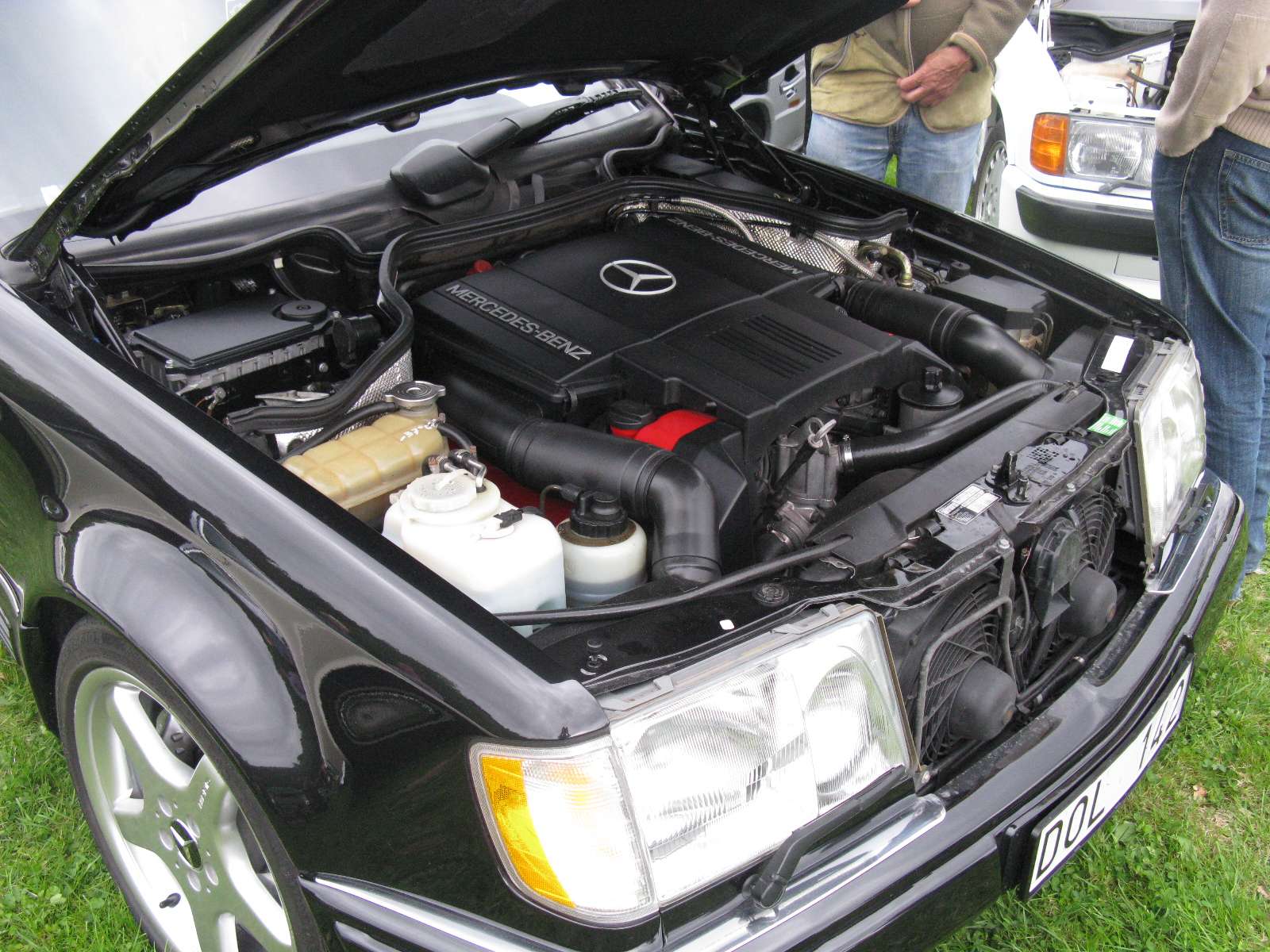 Open hood of a black Mercedes-Benz 500E showing the 5.0-liter M119 V8 engine and cooling system