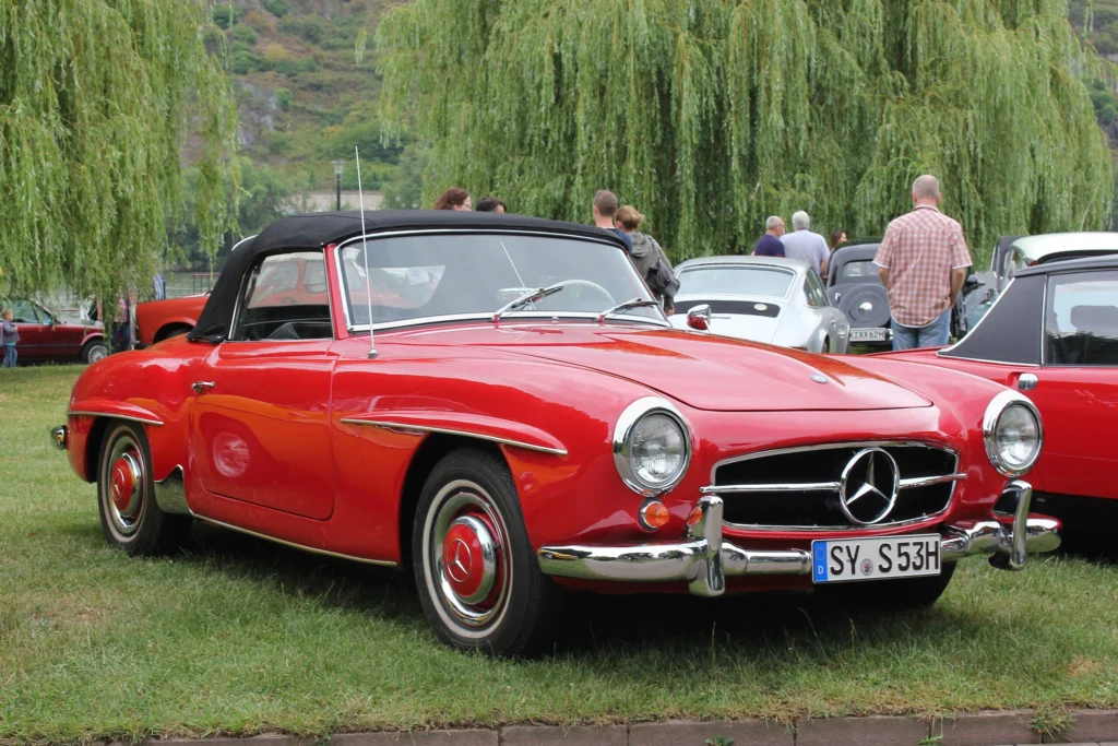 Red Mercedes-Benz 190 SL roadster with a black soft top parked on grass at a classic car show