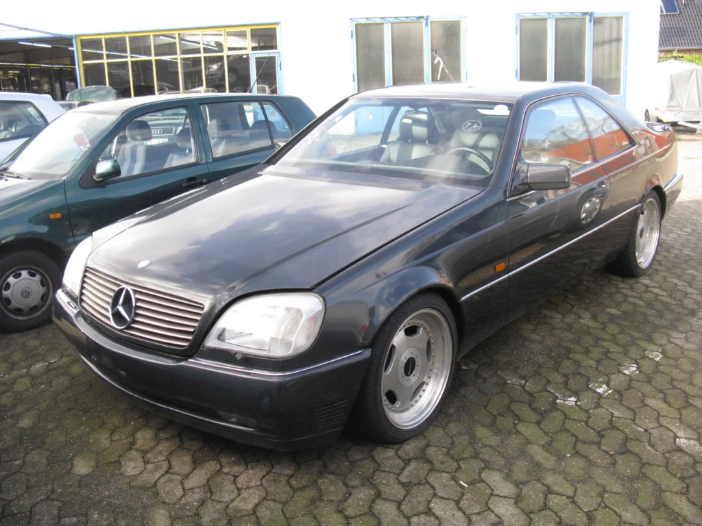 Black Mercedes-Benz 600 SEC C140 coupe parked on cobblestones seen from the front three-quarter