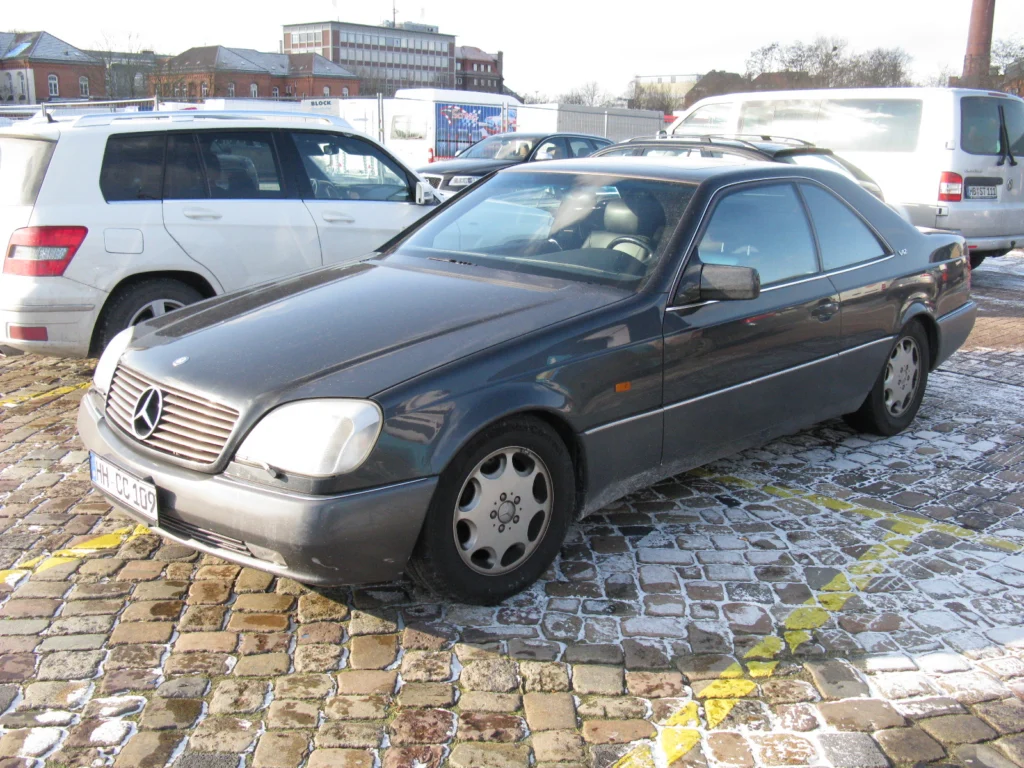 Dark grey Mercedes-Benz 600 SEC coupe parked on a cobbled street in winter