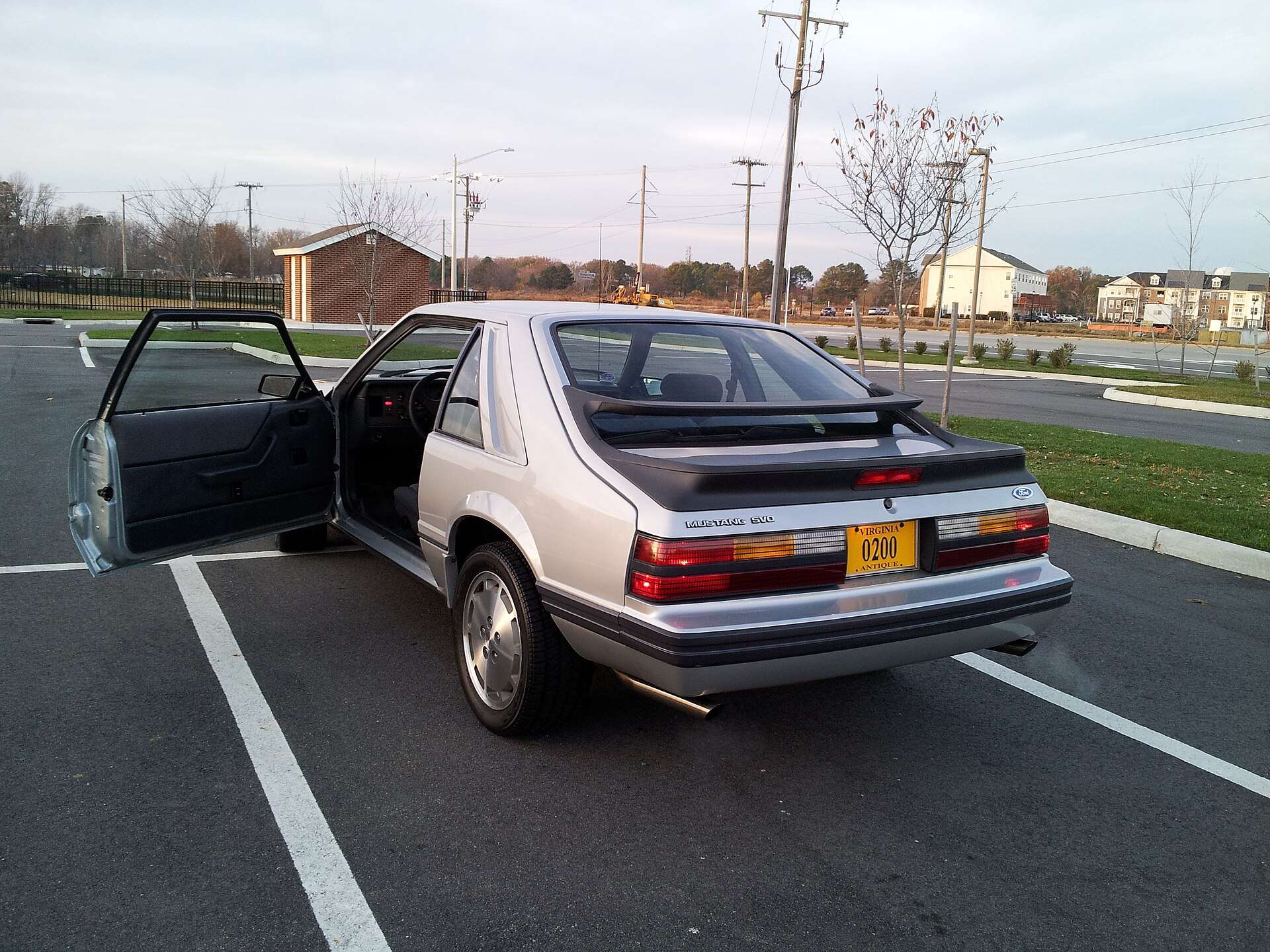 Silver 1986 Ford Mustang SVO seen from the rear with its biplane spoiler and driver door open