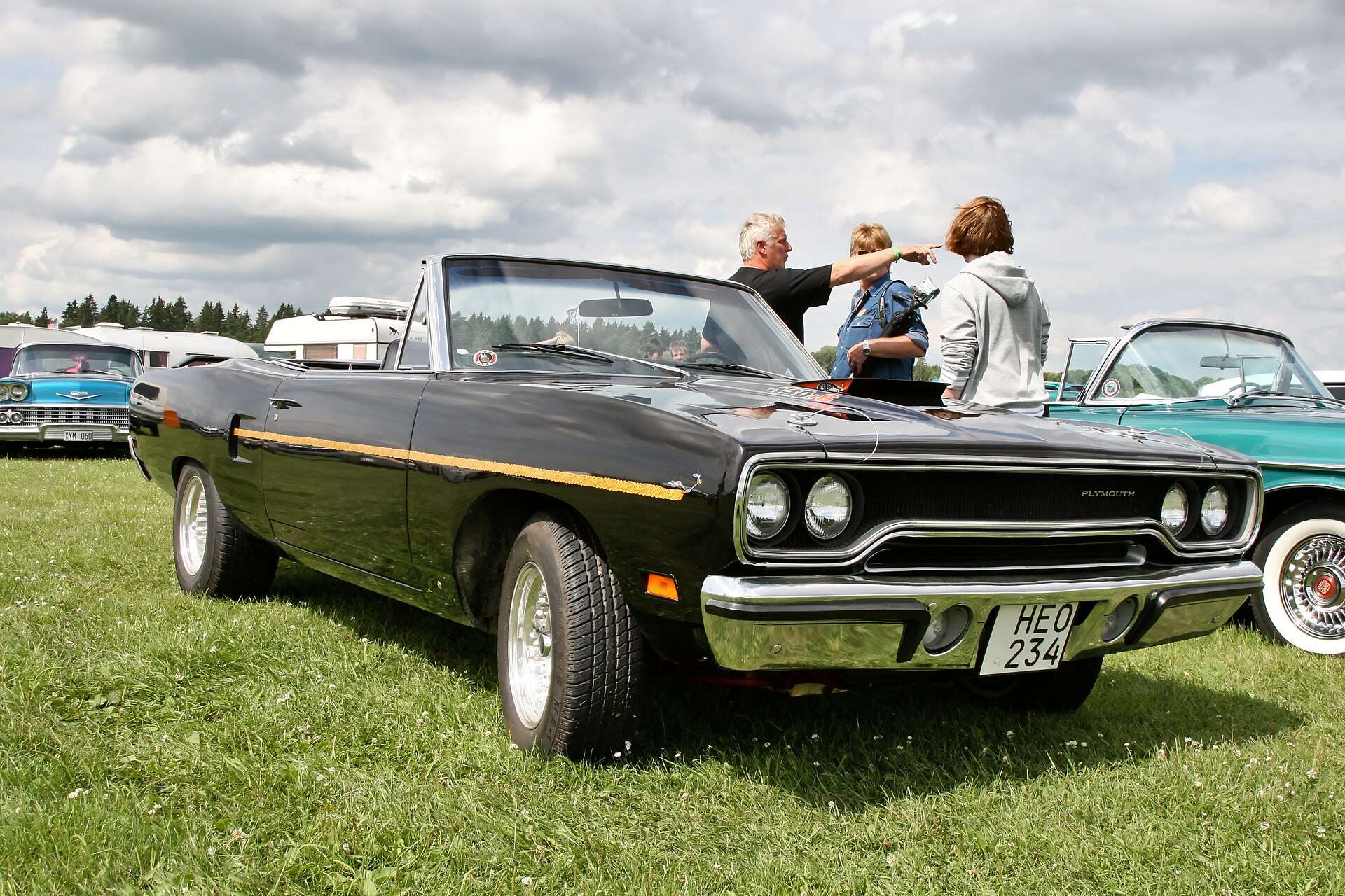 Black Plymouth Road Runner convertible with the top down and a gold side stripe parked on grass at a car show