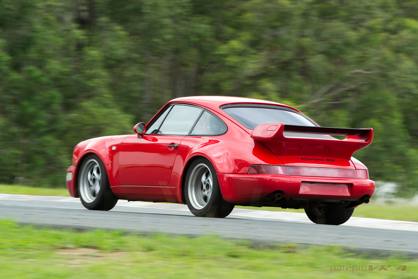 Rear three-quarter view of a red Porsche 964 Carrera RS fitted with the RS 3.8 rear wing on a track