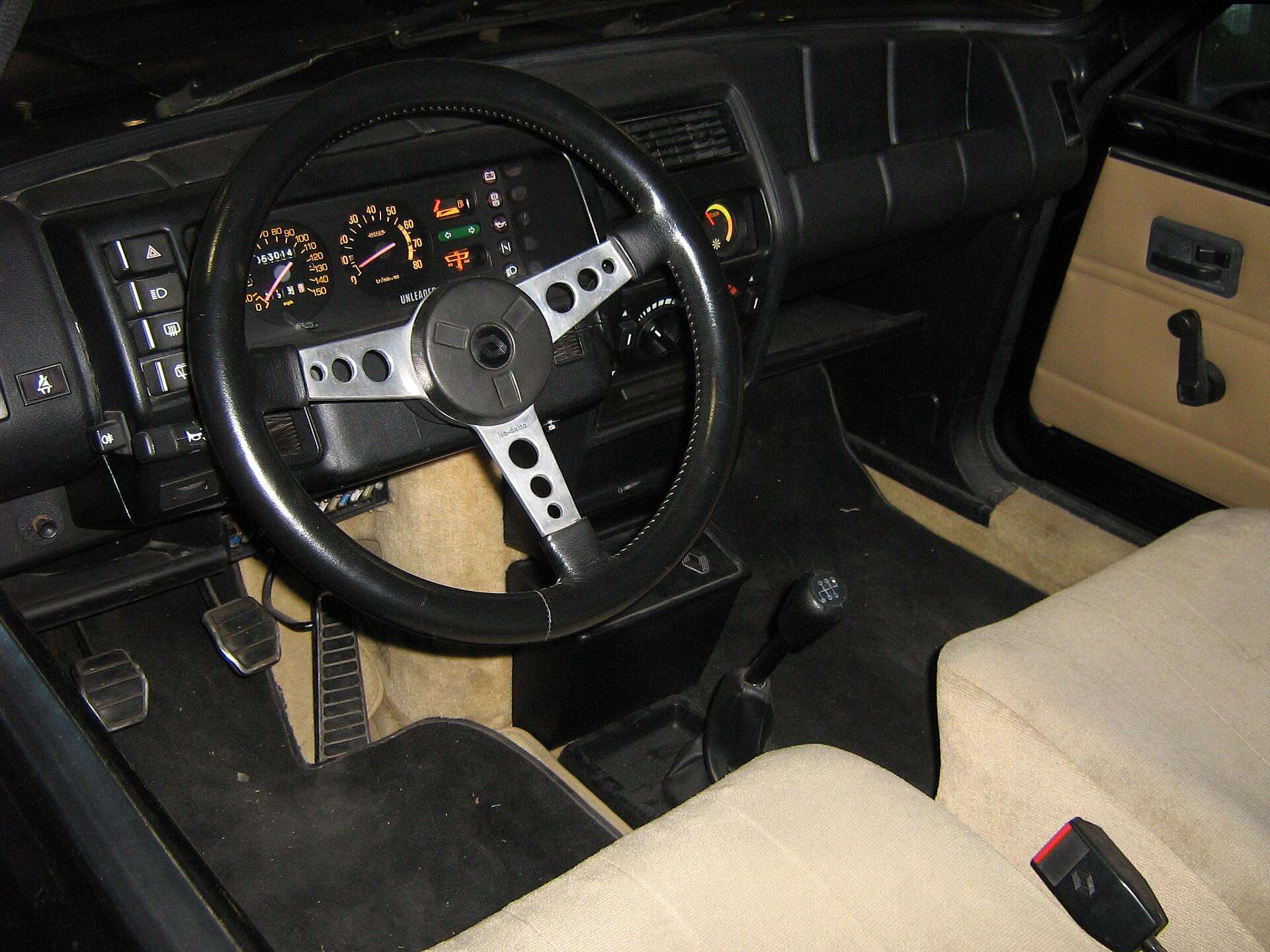 Interior of a 1985 Renault 5 Turbo 2 showing the black dashboard, three-spoke steering wheel and beige seats and door trim