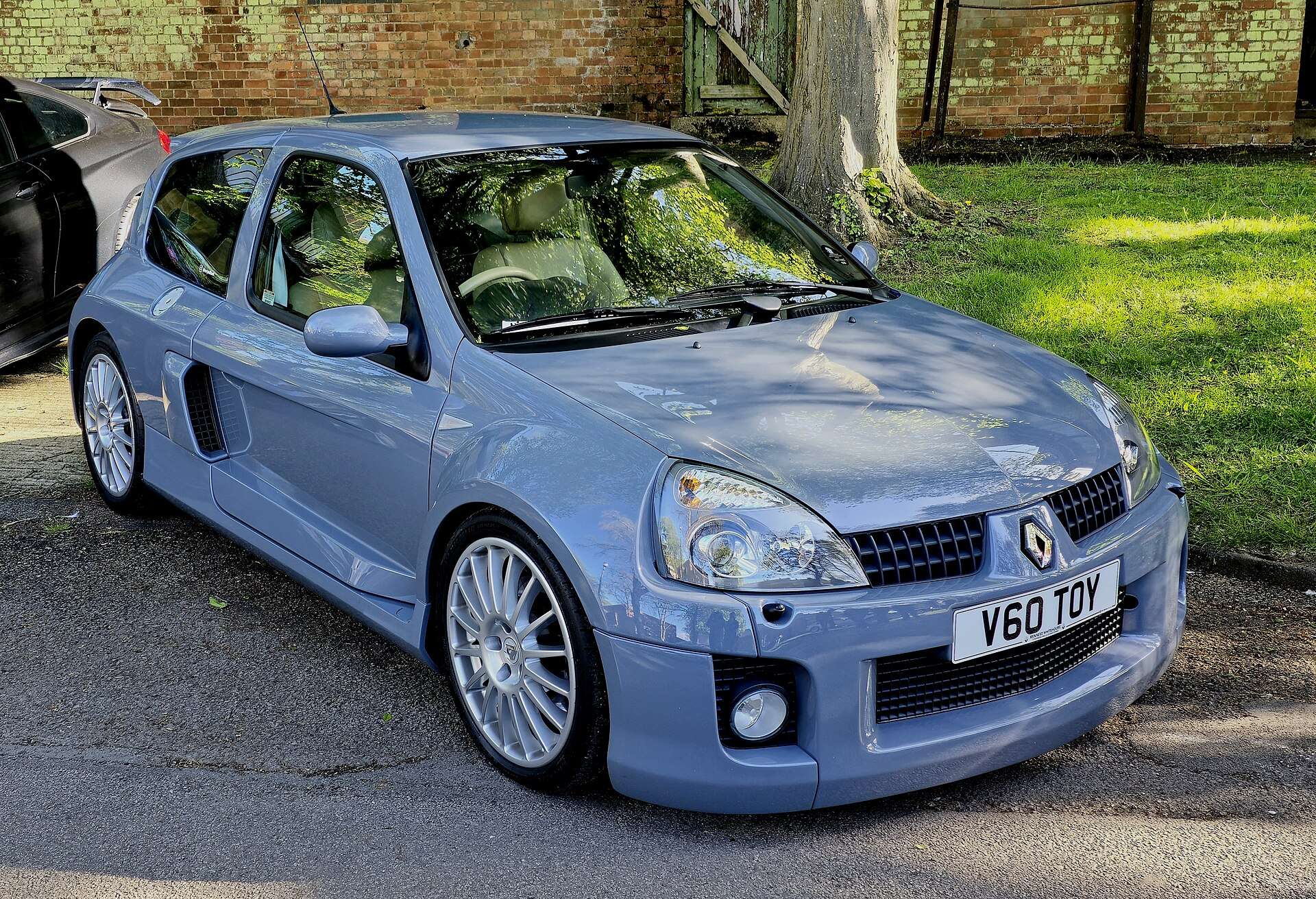 Light blue 2004 Renault Clio V6 Phase 2 with silver wheels parked beside a brick wall