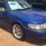 Is the Saab 9-3 Viggen a Future Collector Car? 4,600 Cars, One Turbo Four and a Brand That Can’t Make More Blue 1999 Saab 9-3 Viggen three-door coupe parked at a car show, shown from the front three-quarter with a Swedish flag on the mirror