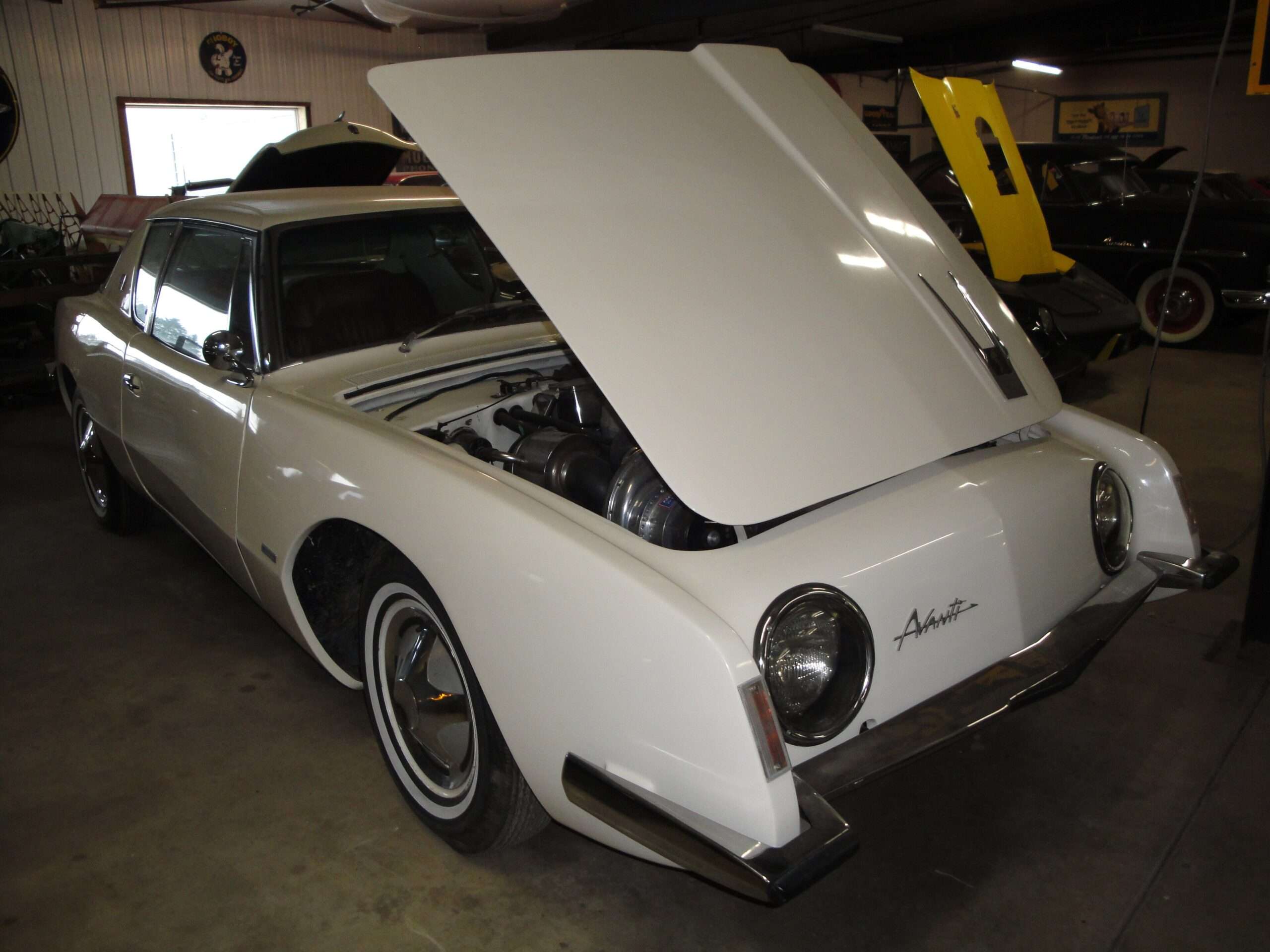 White 1963 Studebaker Avanti with its hood raised to show a supercharged V8 engine bay