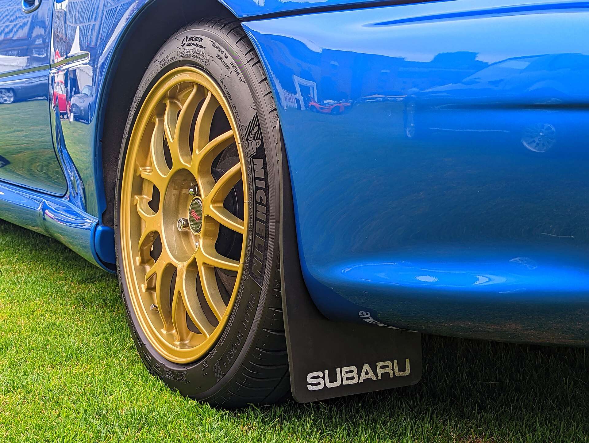 Close-up of a gold BBS alloy wheel and Subaru mudflap under the widened blue front fender of a 22B STi