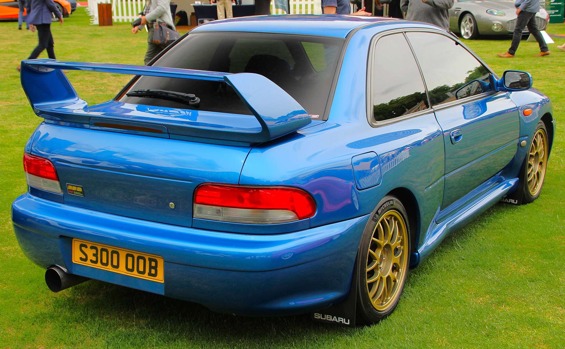 Rear view of a blue Subaru Impreza 22B STi with its tall adjustable rear wing, wide rear fenders and gold wheels