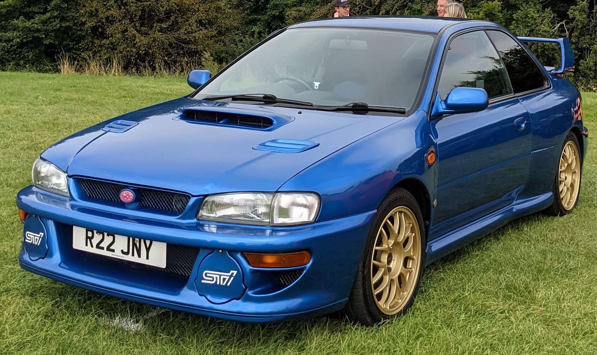 Blue right-hand-drive 22B STi coupe with gold wheels parked on a lawn, photographed from the front three-quarter