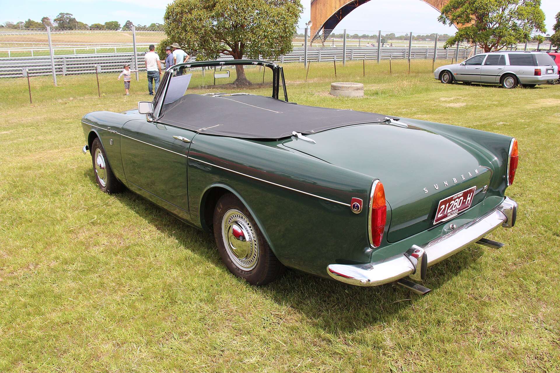 Dark green 1966 Sunbeam Tiger roadster with black tonneau cover and chrome bumpers parked on a grass field