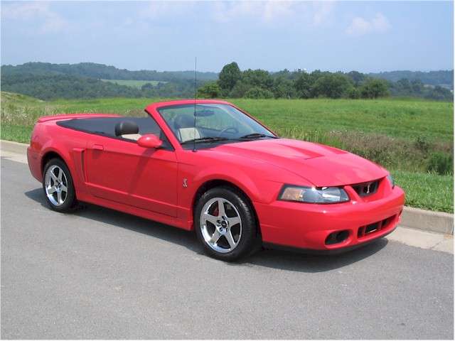 Torch Red 2003 Ford Mustang SVT Cobra convertible with the top down, parked beside a green hillside