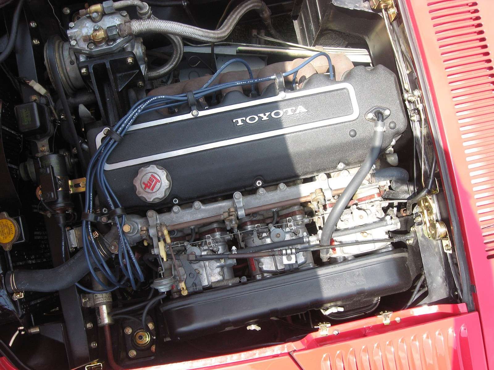 Engine bay of a red Toyota 2000GT MF12 with the 2.3-liter 2M single-overhead-cam six and triple carburetors