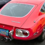 Red Toyota 2000GT coupe seen from the rear three-quarter, showing the fixed roof of the production closed body