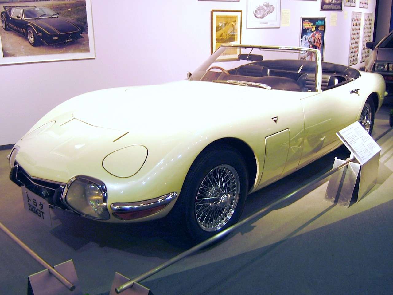 Cream-colored open Toyota 2000GT convertible without a roof, displayed in a museum in the style of the James Bond film car