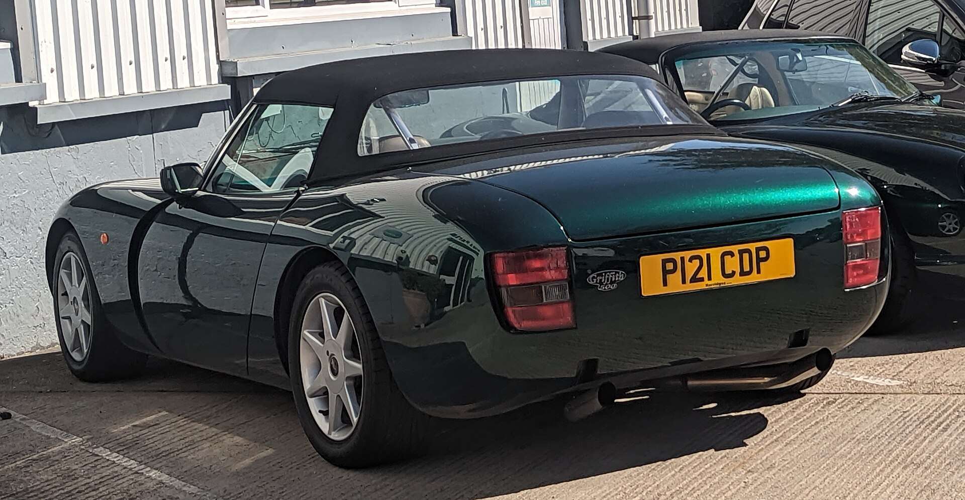 Rear three-quarter view of a dark green TVR Griffith 500 roadster with its soft top raised