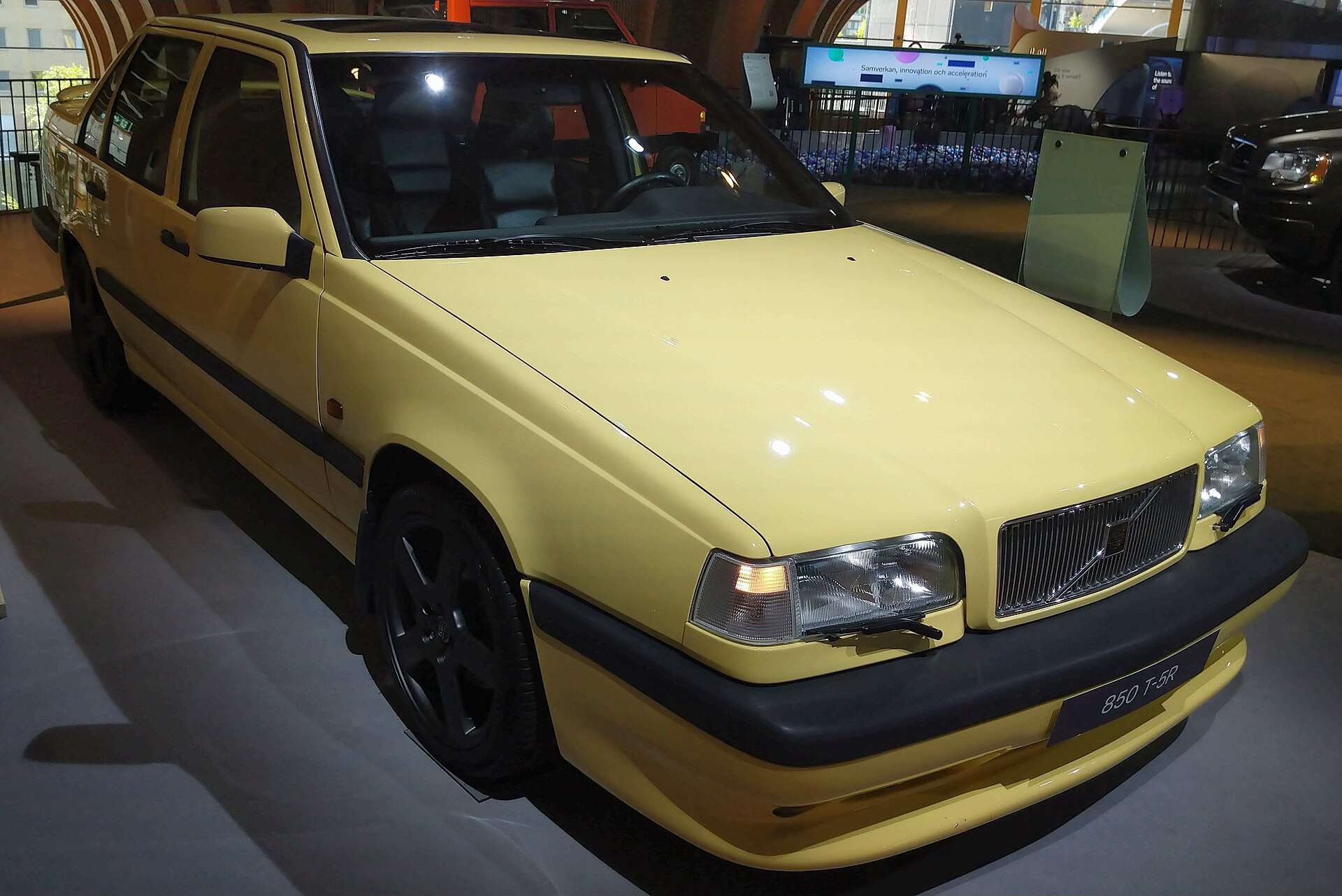 Front three-quarter view of a Cream Yellow Volvo 850 T-5R estate displayed indoors at World of Volvo 2024